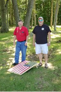 Two men standing outside playing Corn Hole
