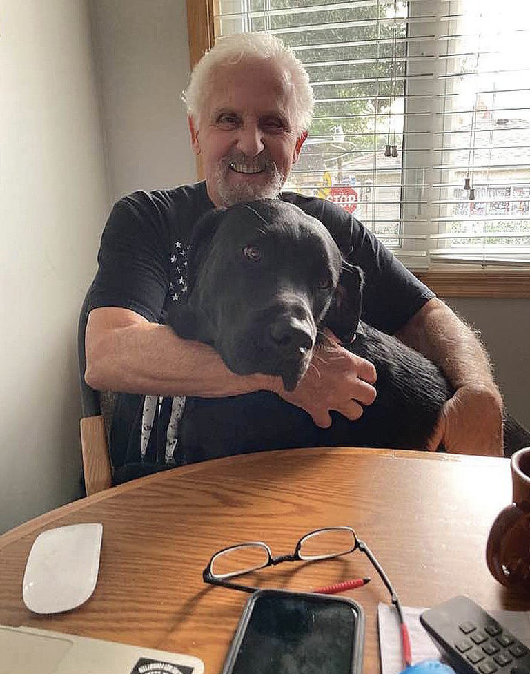 A smiling man holding a Black Labrador dog