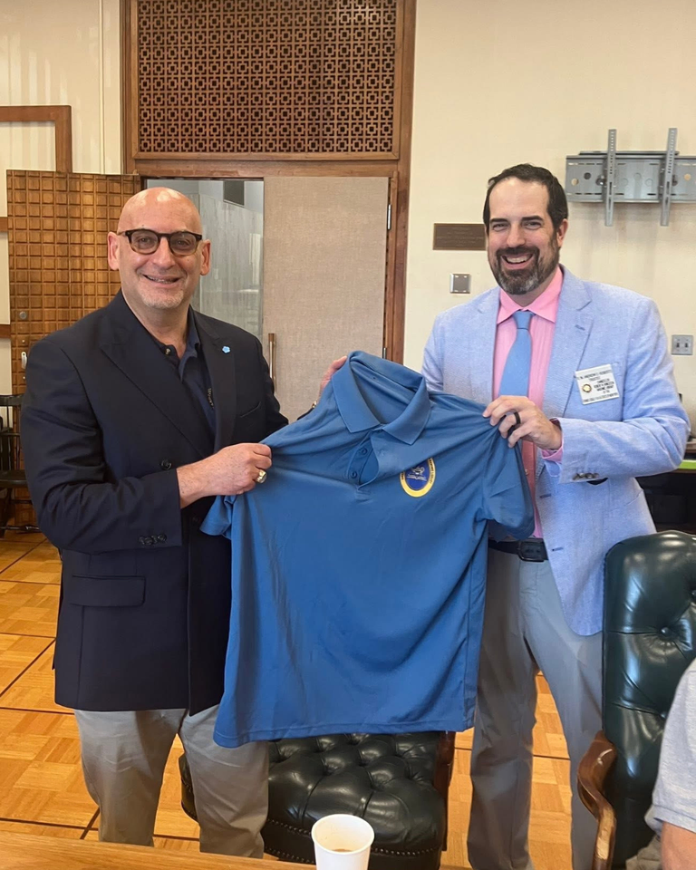 Two men smiling and standing together holding up a blue Livingston Library polo