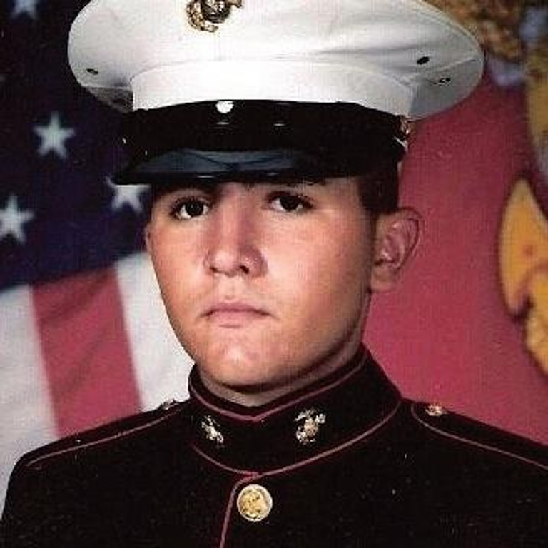 A young military man in uniform standing in front of an American flag