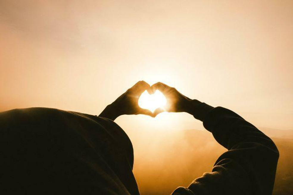 person with hands in a heart shape holding hands up to the sun