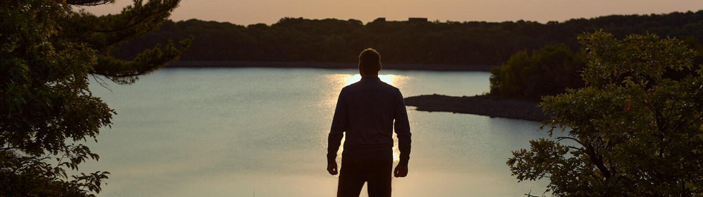 Man looking at a lake with trees in the distance