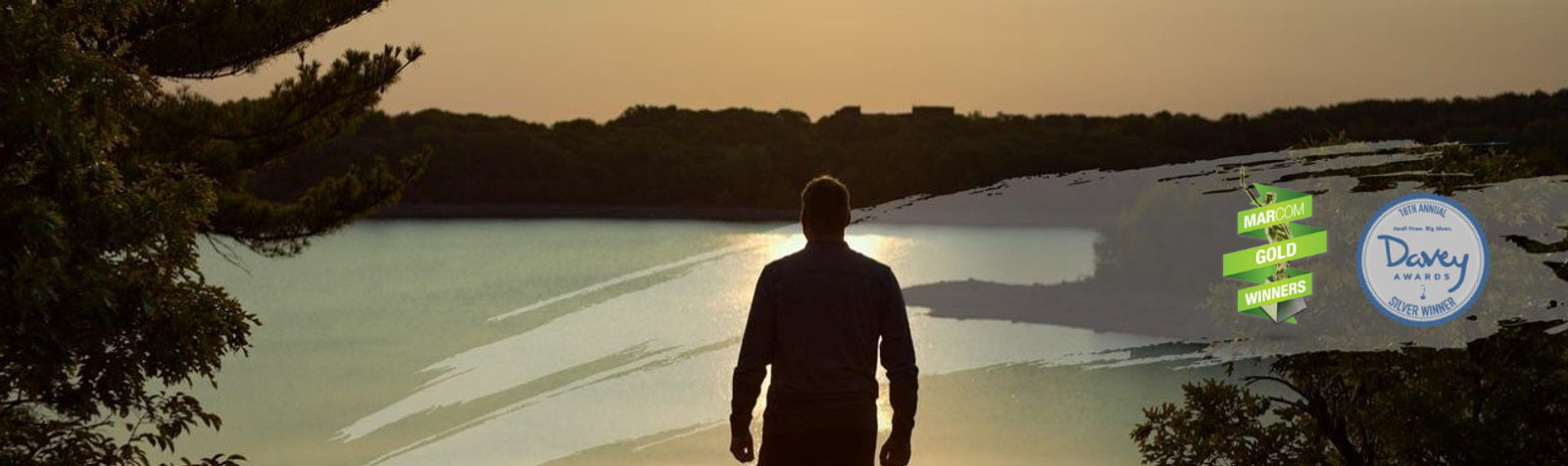 man looking out at landscape of a sunrise, davey awards logo and marcom award logo