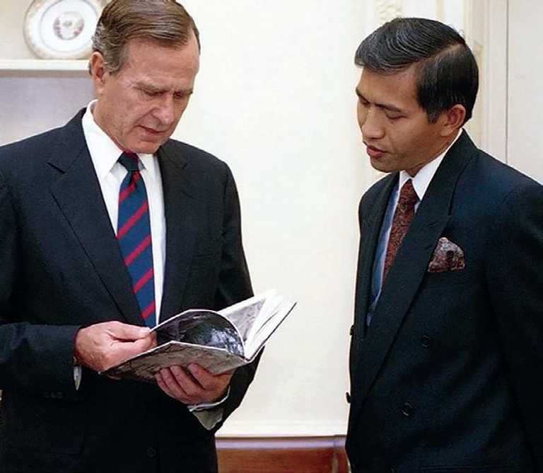 Two men dressed in black suits stand beside each other reading a book