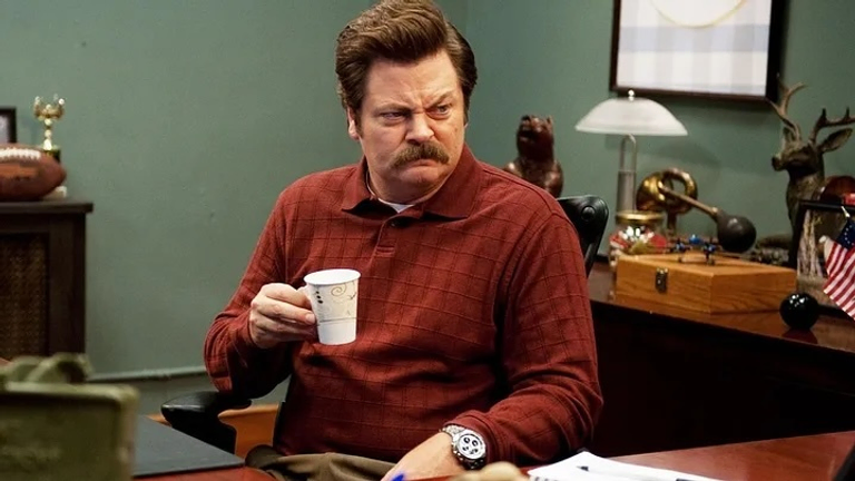 Ron Swanson from Parks and Recreation sitting at his desk holding a cup of coffee