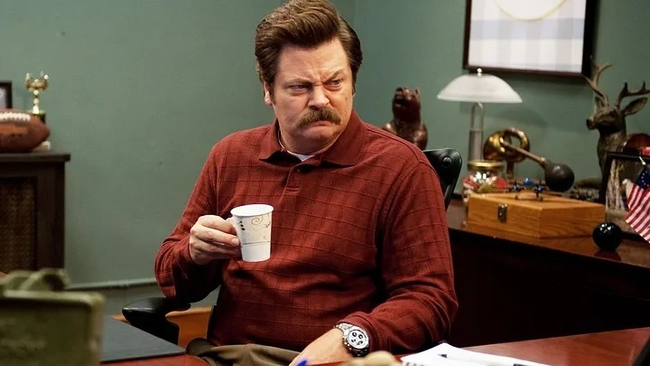 Ron Swanson from Parks and Recreation sitting at his desk holding a cup of coffee