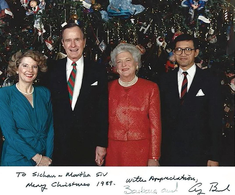 Two women, dressed in blue and red formal attire, and two men, dressed in black suits, pose for a photo in front of a Christmas tree