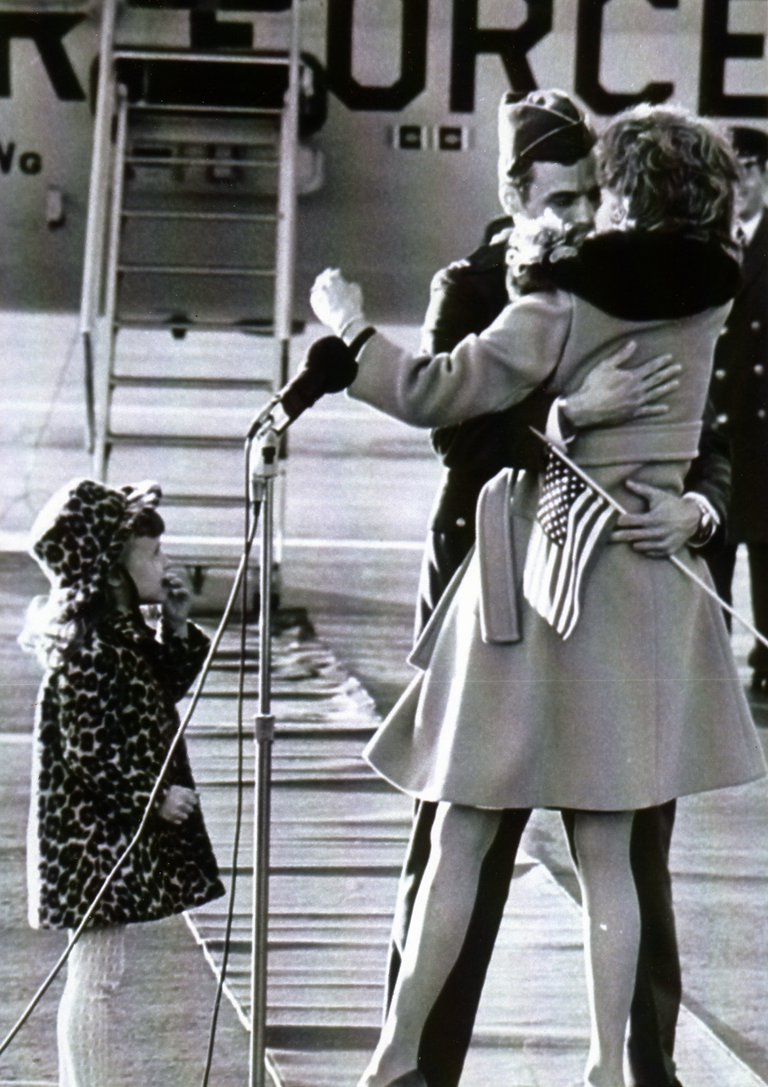 A soldier is welcomed home by his wife and daughter outside an airplane