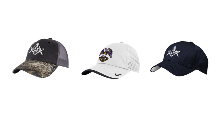 Three baseball caps, one adorned with camouflage and the square and compasses, one white one adorned with the double-headed eagle, and one navy blue one adorned with the square and compasses