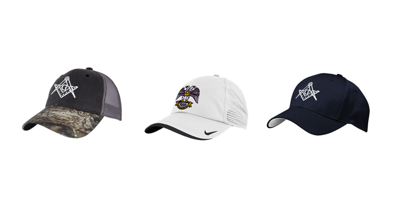 Three baseball caps, one adorned with camouflage and the square and compasses, one white one adorned with the double-headed eagle, and one navy blue one adorned with the square and compasses