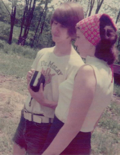 An image of a young man and young woman standing outside with trees in the background.