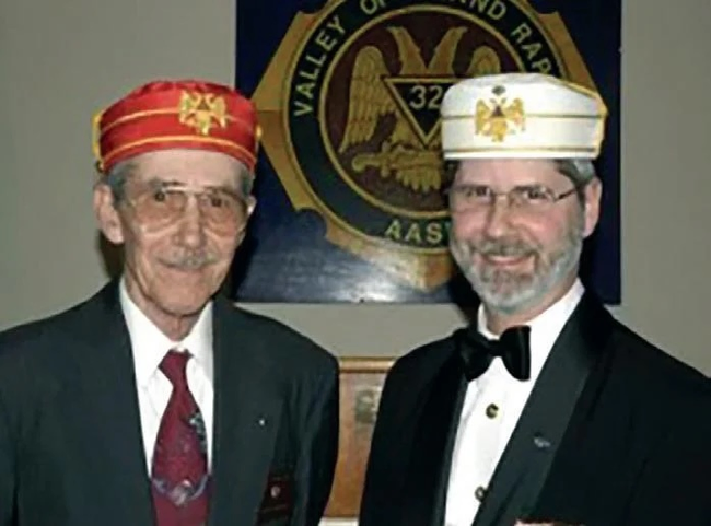 A father and son standing together both wearing a Scottish Rite cap.