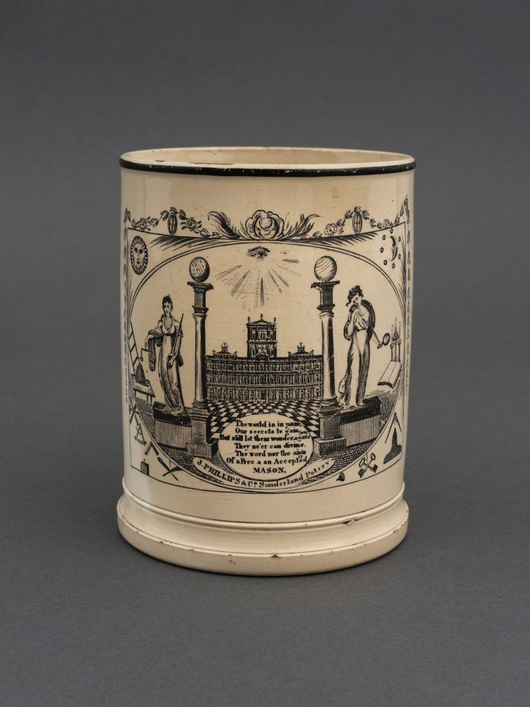An antique mug adorned with Masonic symbols like the columns and the eye of providence