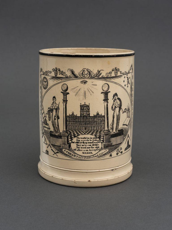 An antique mug adorned with Masonic symbols like the columns and the eye of providence