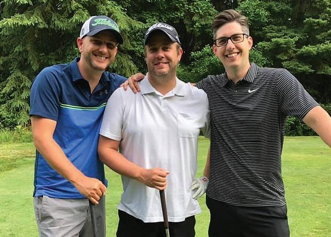 Three men standing together on a golf course looking at the camera.