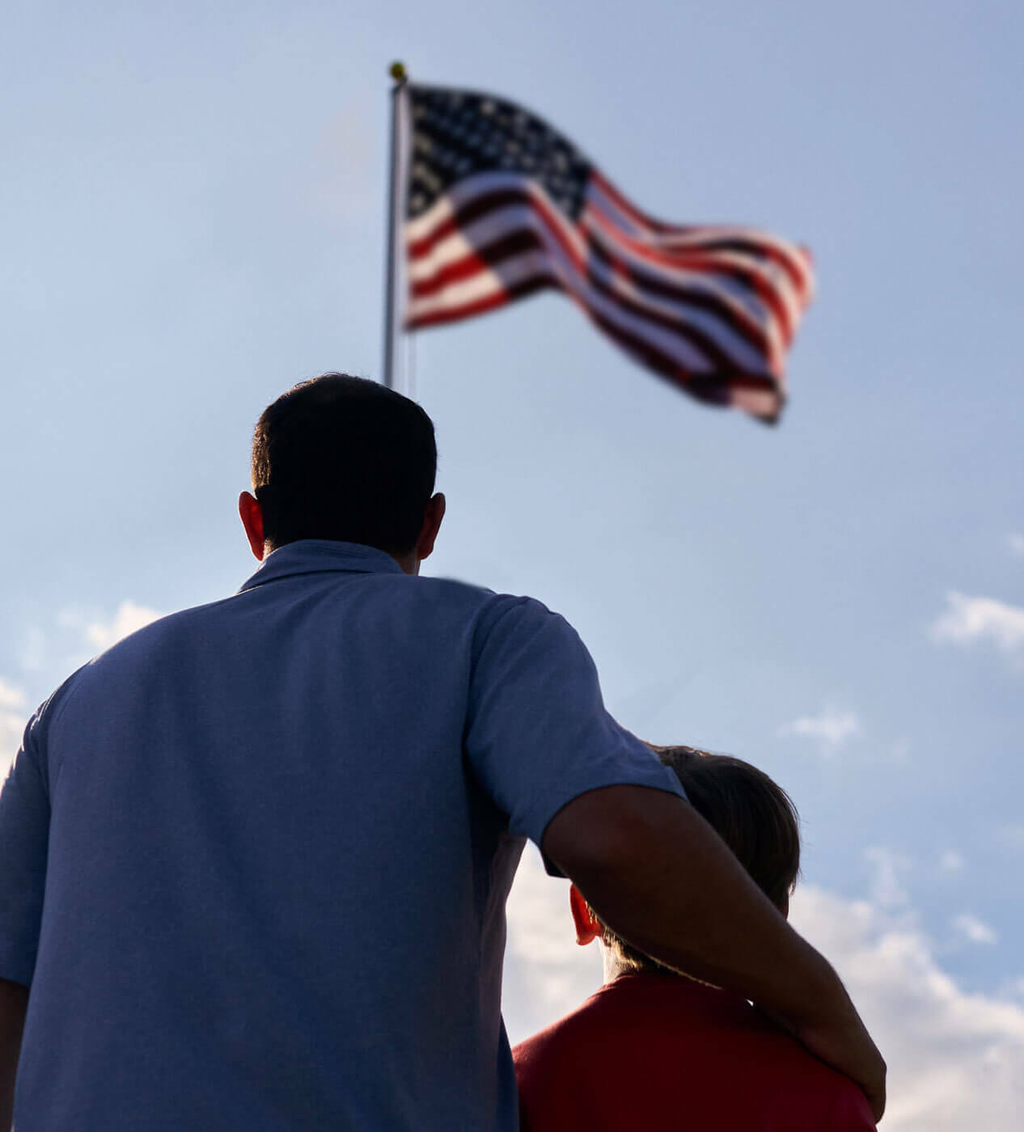 father and son looking up at the raised American flag