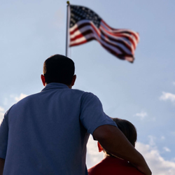 father and son looking up at the raised American flag