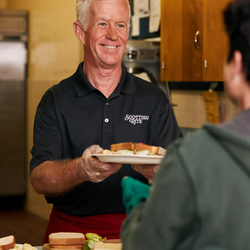 Scottish Rite man handing someone a sandwich at a soup kitchen