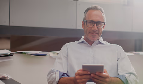 man in office looking at camera with tablet in hand