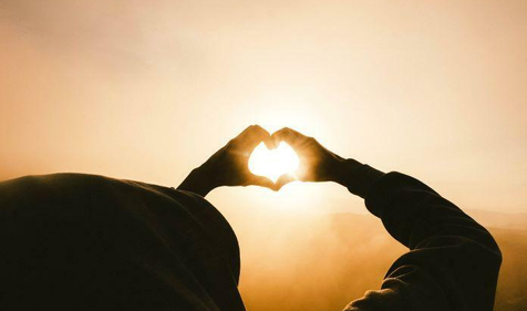 person holding their hands in a heart shape up to the light