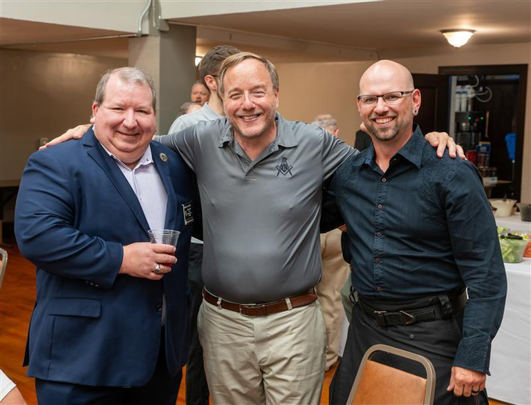 Three smiling men in business casual attire with their arms around each other for a photo