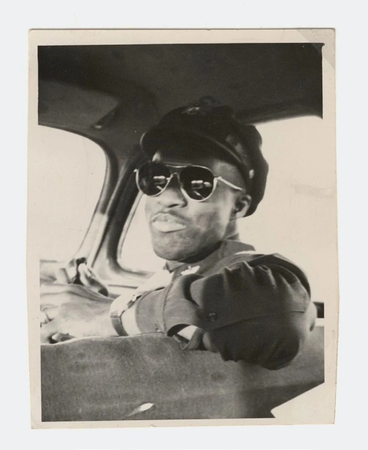 A man in sunglasses and a pilot uniform sitting in the front of a plane