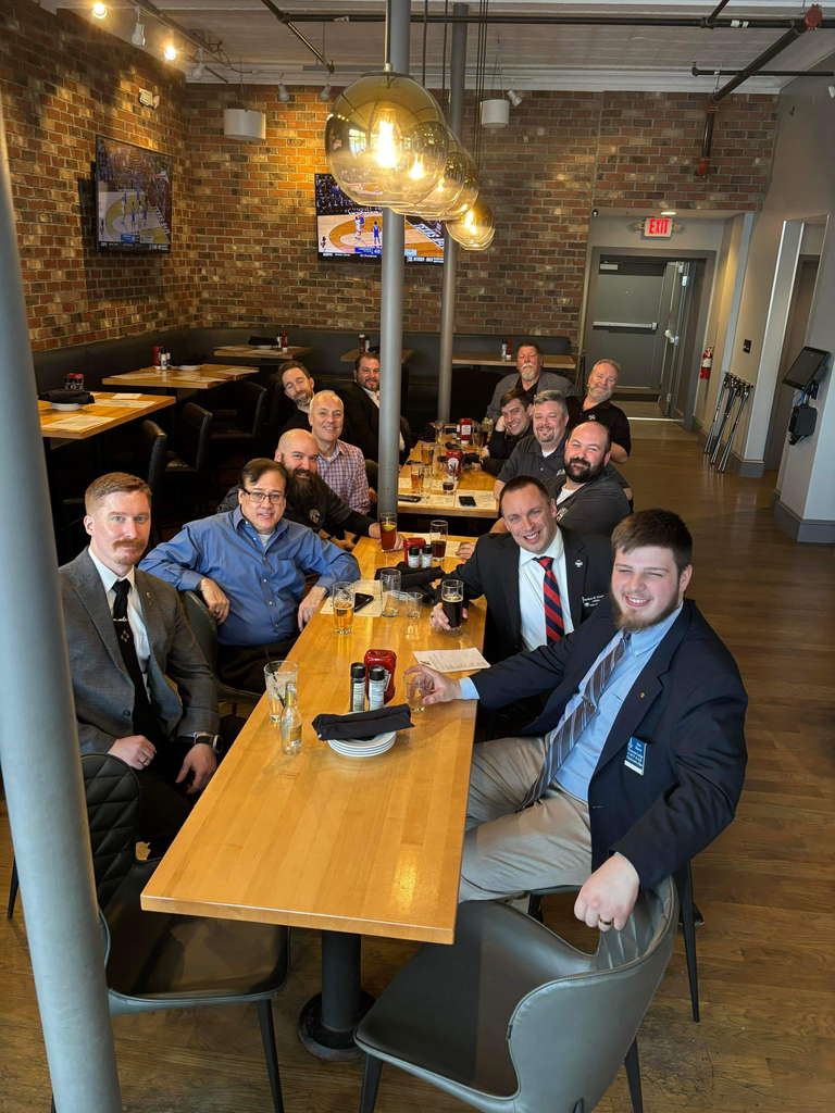 A group of smiling Freemasons sitting at a restaurant table smiling at the camera