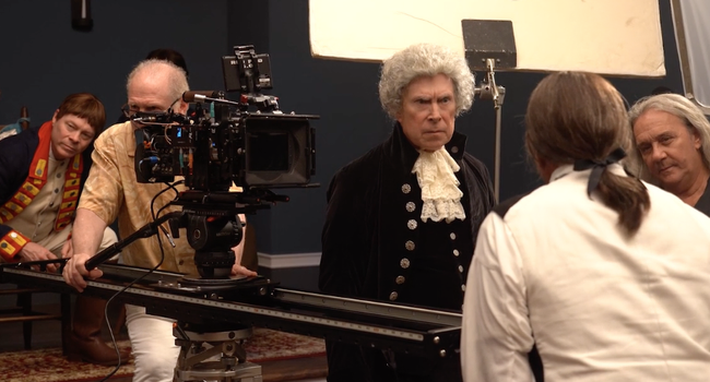 A man with a professional movie camera filming two men dressed in colonial attire