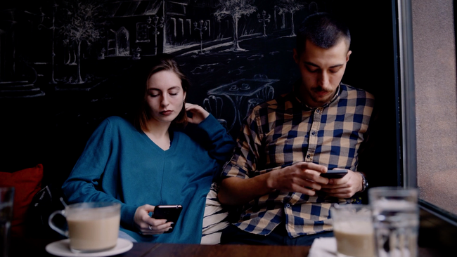 A millennial man and women sitting in a café using their cell phones