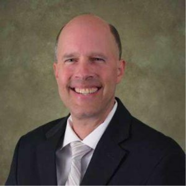 A professional headshot of a man smiling and wearing a suit