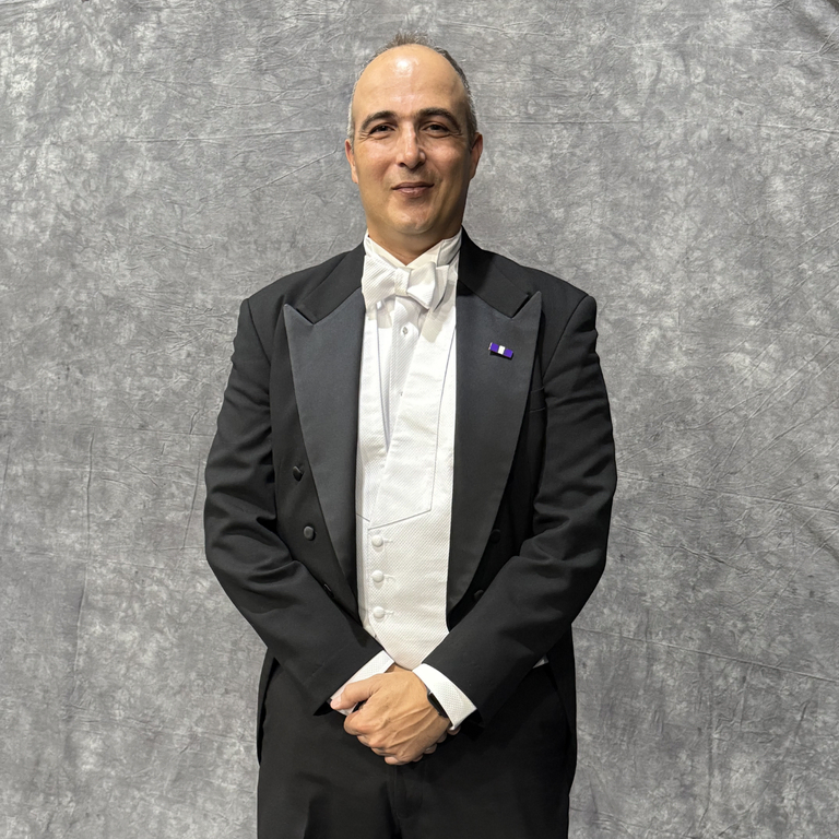 A smiling Scottish Rite Mason standing and dressed as a 33° candidate in a black suit, white shirt, and purple pin