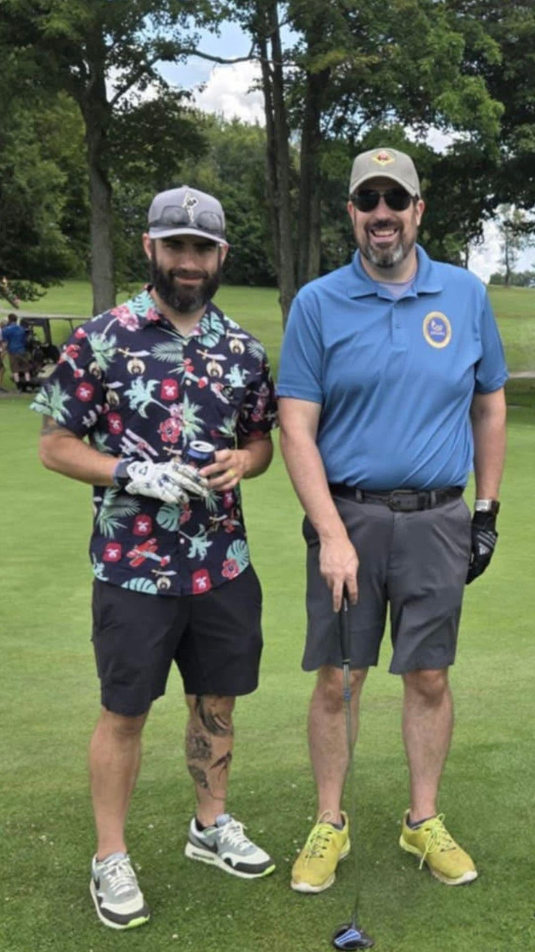 Two men standing together on a golf course smiling for the camera
