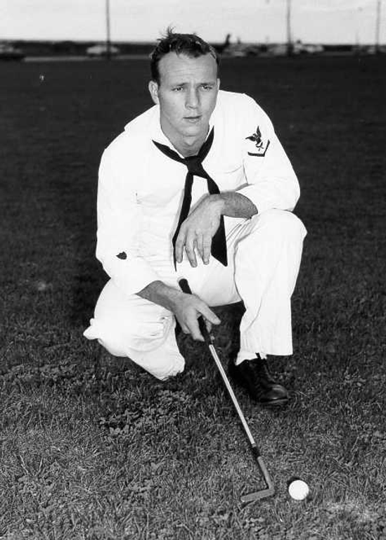 Arnold Palmer kneeling in his Coast Guard uniform in front of a golf ball, holding a golf club