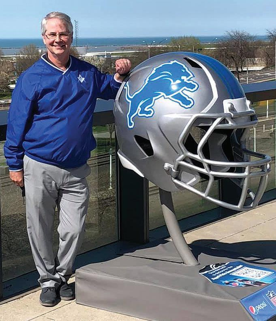 A man posing next to a statue of a Detroit Lions football team helmet