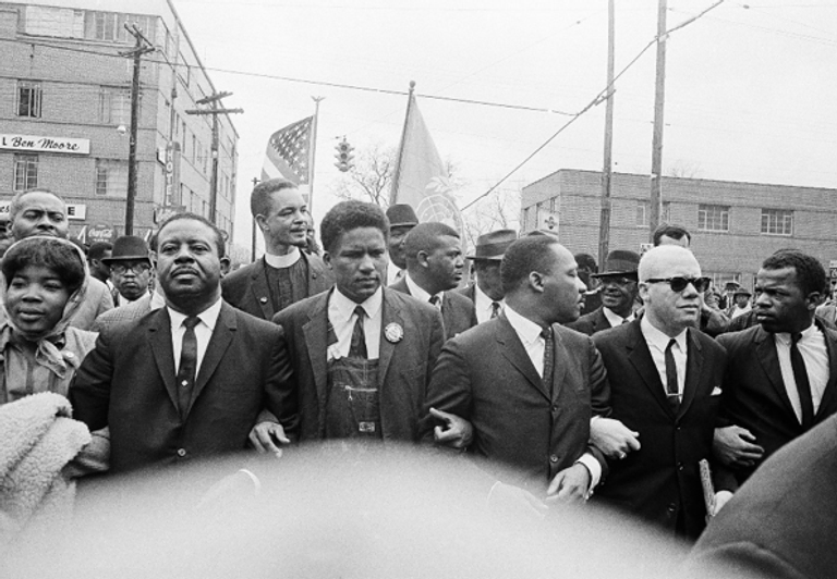 Dr. Martin Luther King Jr. locks arms with Rev. Ralph Abernathy, James Foreman, King, Jesse Douglas Sr., and John Lewis as they lead a crowd on a march through the streets of